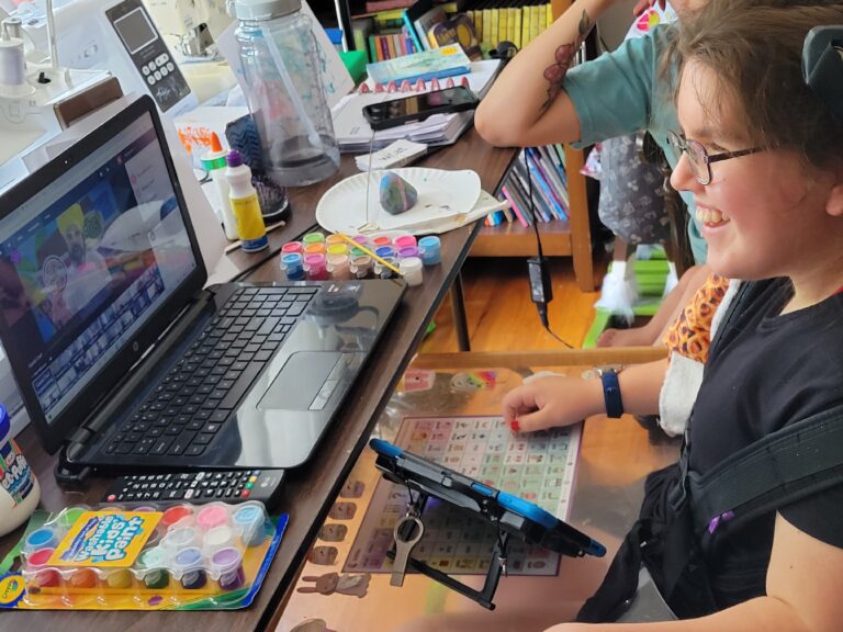 Variety Kid smiling and doing arts and crafts through a virtual program.