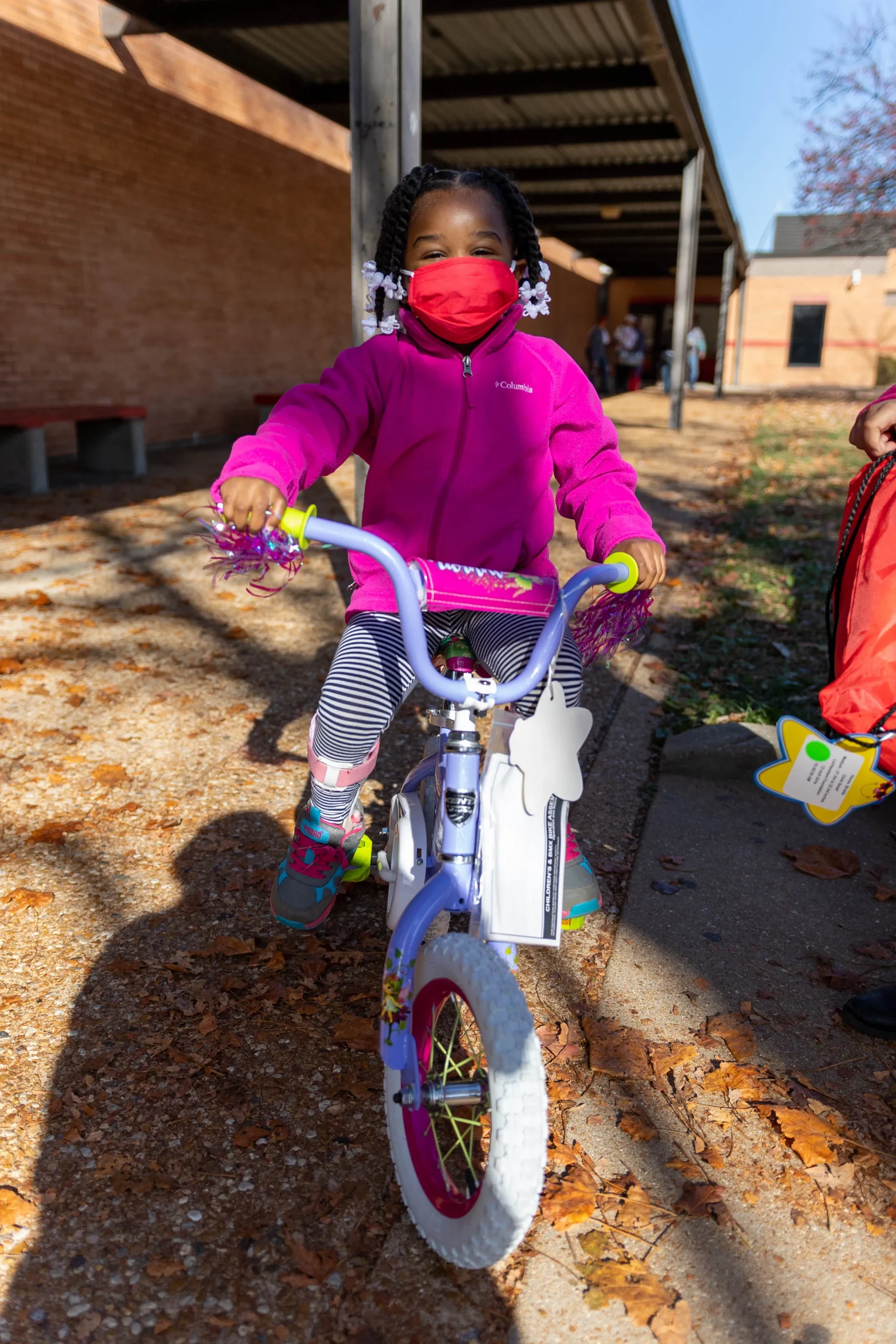 A little girl wearing a face mask is riding her bike into the camera.