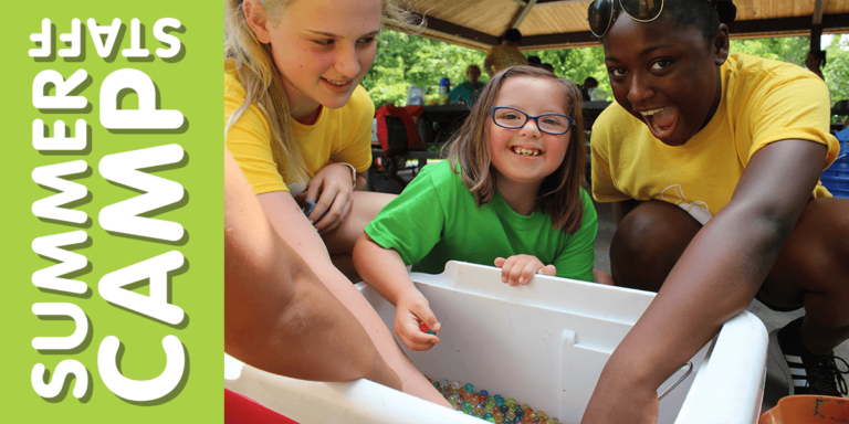 Two camp counselors are engaging in a sensory activity with a young camp attendee.